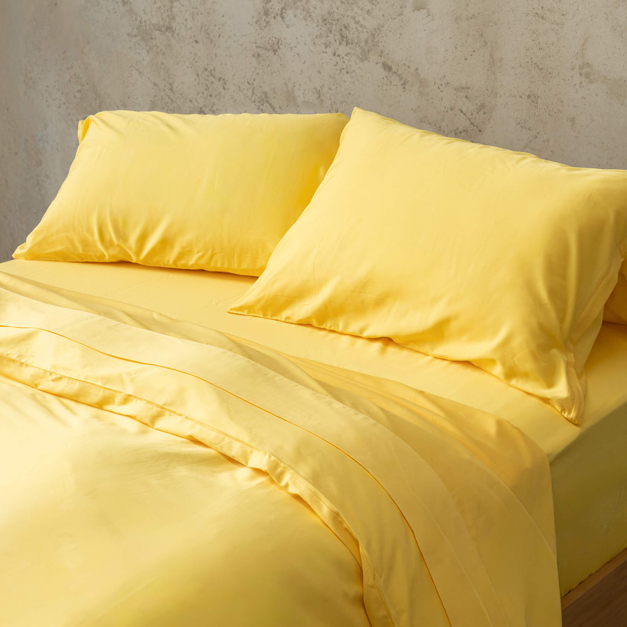 Bright yellow duvet cover set on a bed, against a neutral concrete look backdrop.
