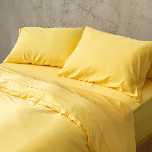 Bright yellow duvet cover set on a bed, against a neutral concrete look backdrop.