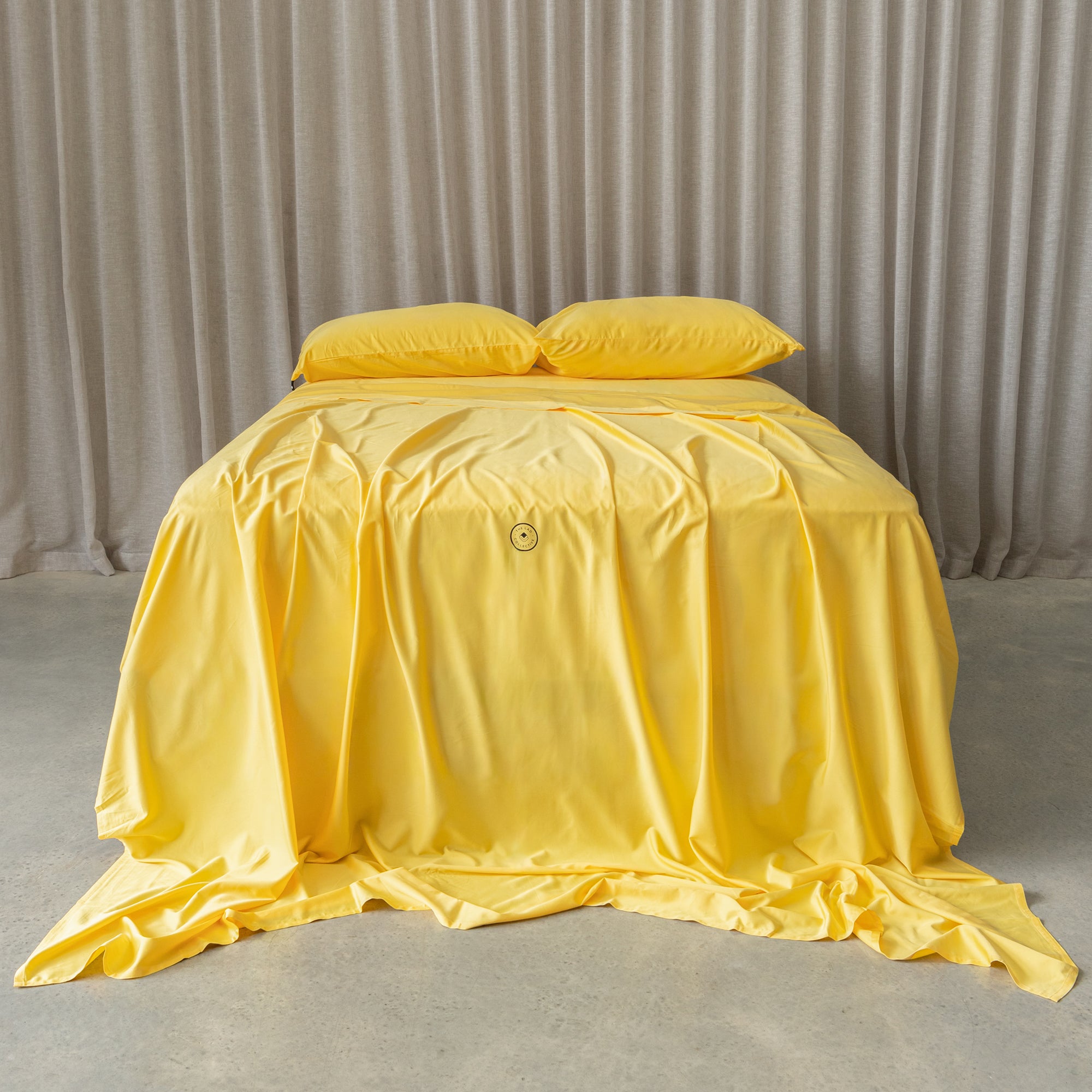 Bright yellow bedding set on a bed, against a neutral background and a beige curtain. 