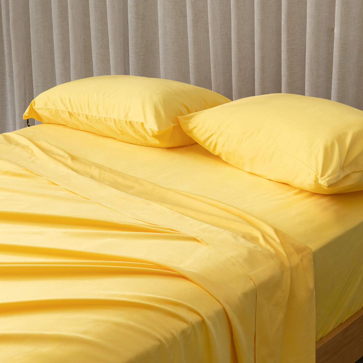 Close-up of bright yellow bedding set on a bed, against a beige curtain. 