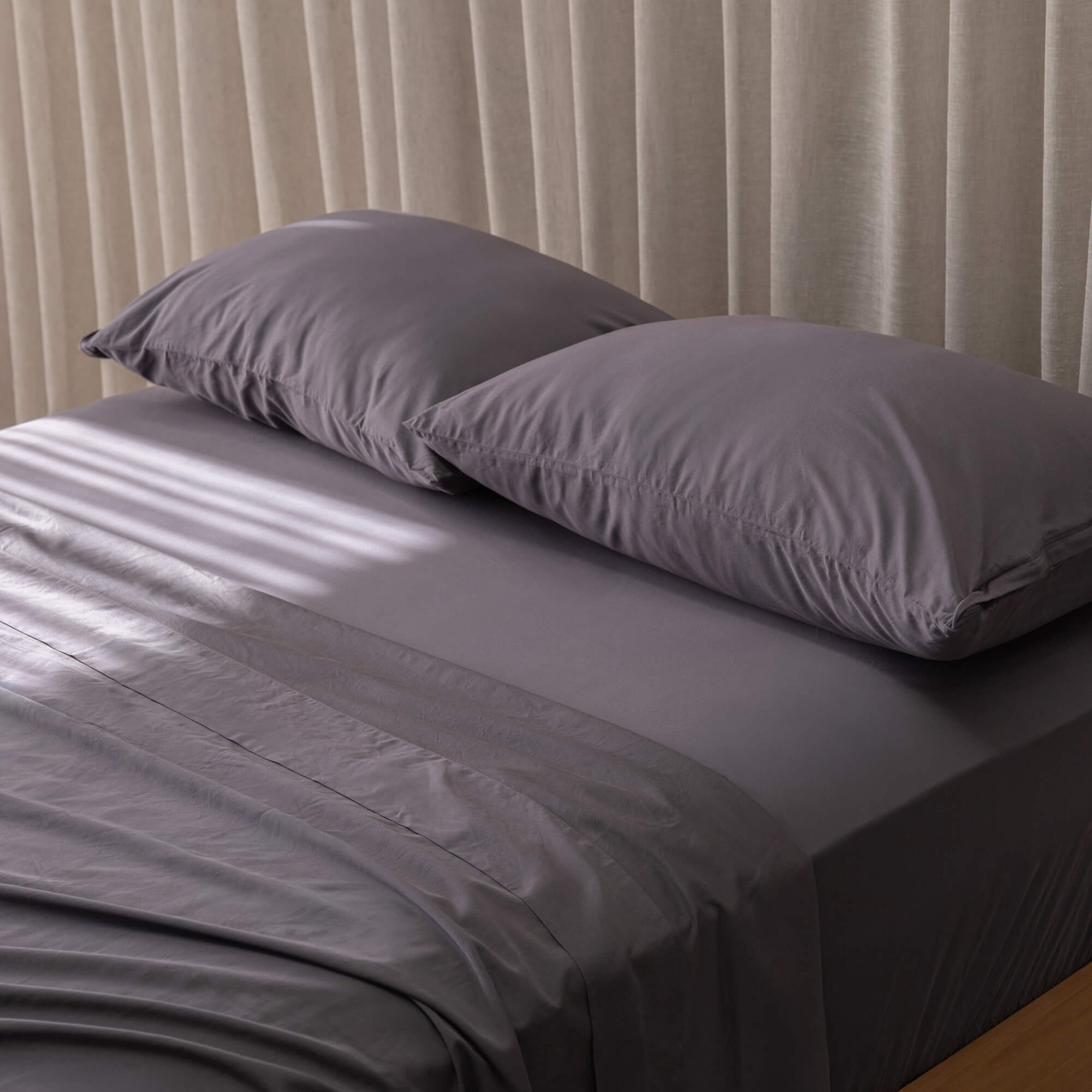 Gray bedspread on a bed with white pillows against a beige curtain background