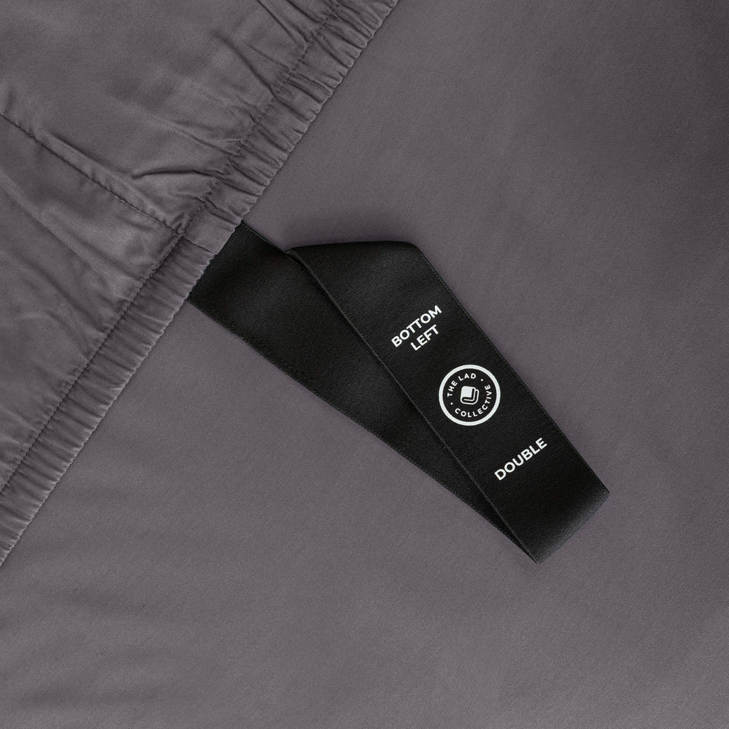 Close up of corner strap of fitted sheet in grey coloured bedding
