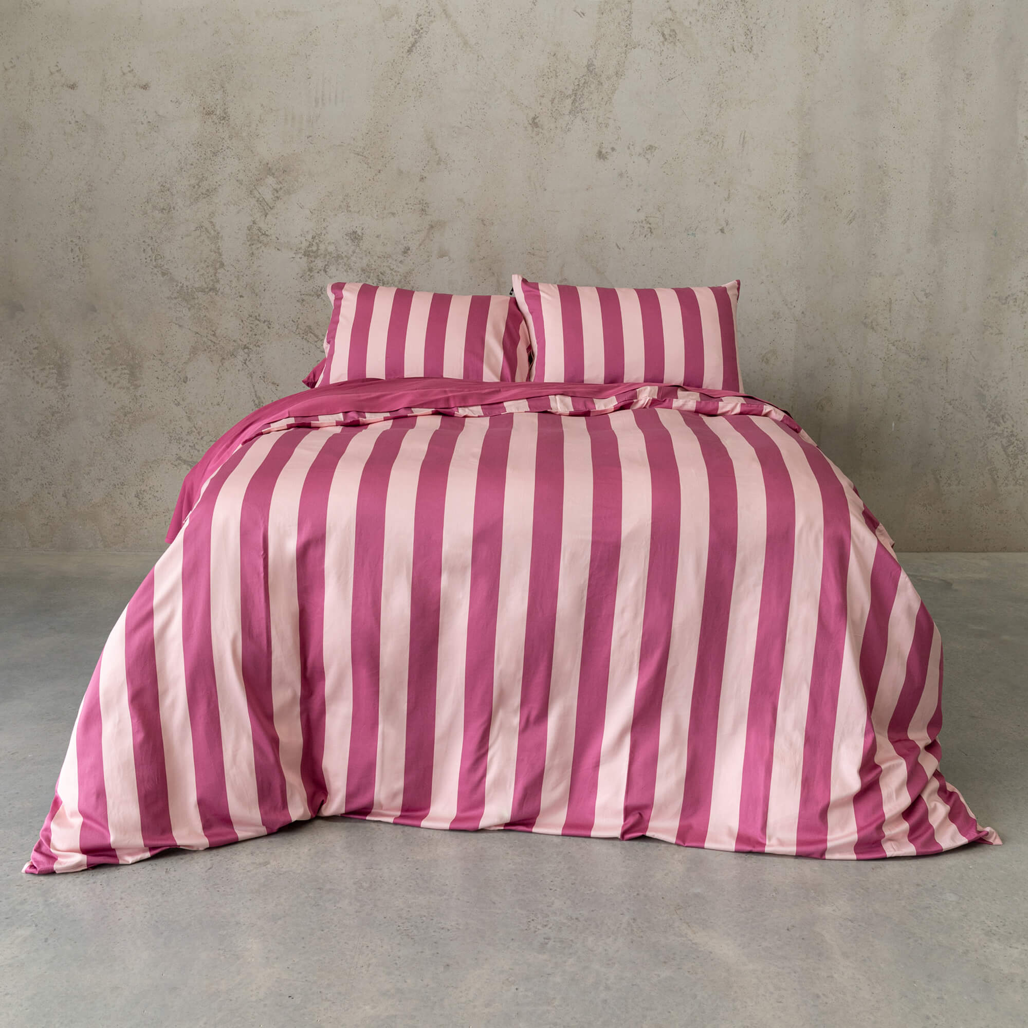 Raspberry pink stripe duvet cover set on a bed, against a neutral concrete look backdrop. 