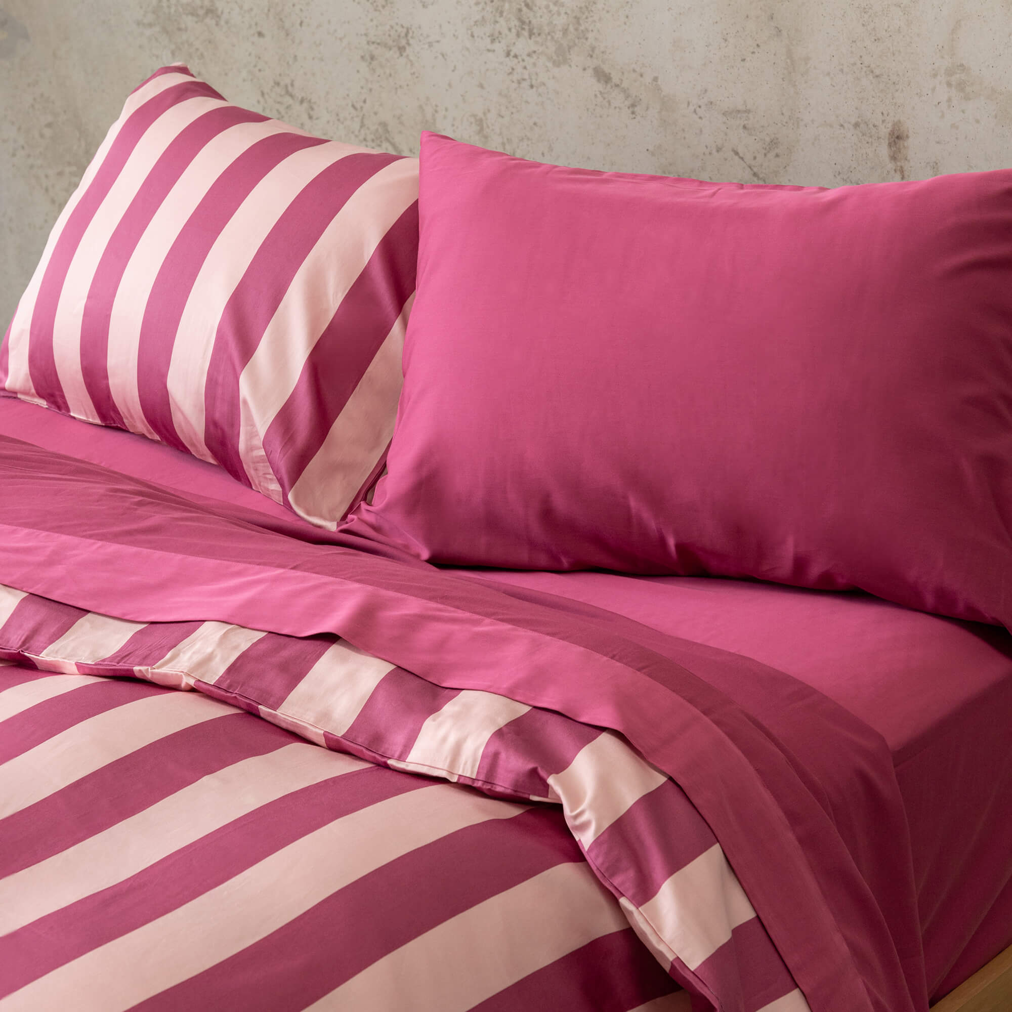 Raspberry pink stripe duvet cover set on a bed, against a neutral concrete look backdrop. 