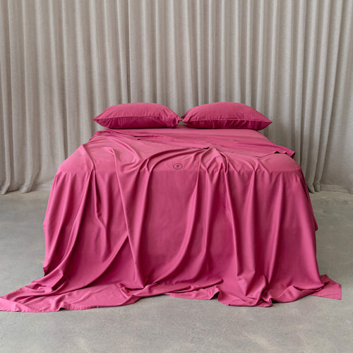 Raspberry pink bedding set on a bed, against a neutral background and beige curtains. 