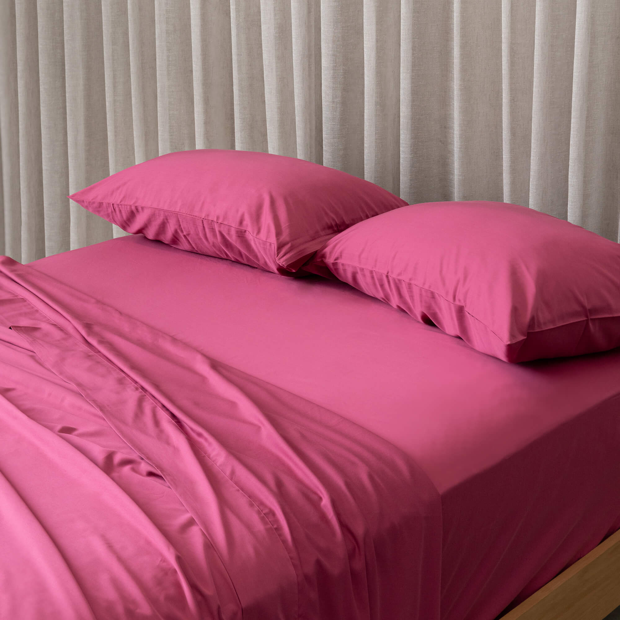 Raspberry pink bedding set on a bed, against a neutral background and beige curtains. 