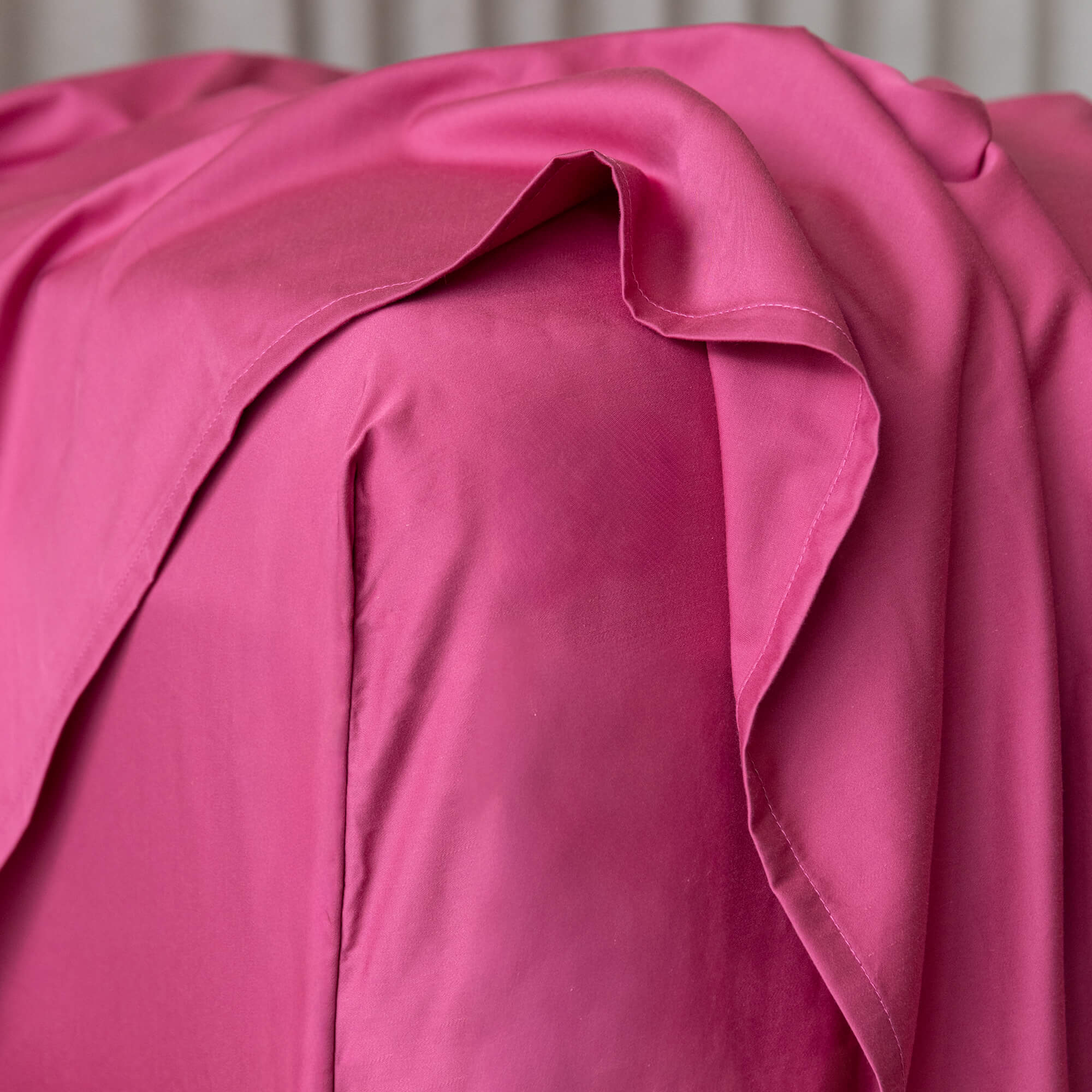 Close up of a raspberry pink fitted sheet on a bed, featuring the corner of the fitted sheet.