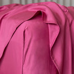 Close up of a raspberry pink fitted sheet on a bed, featuring the corner of the fitted sheet.