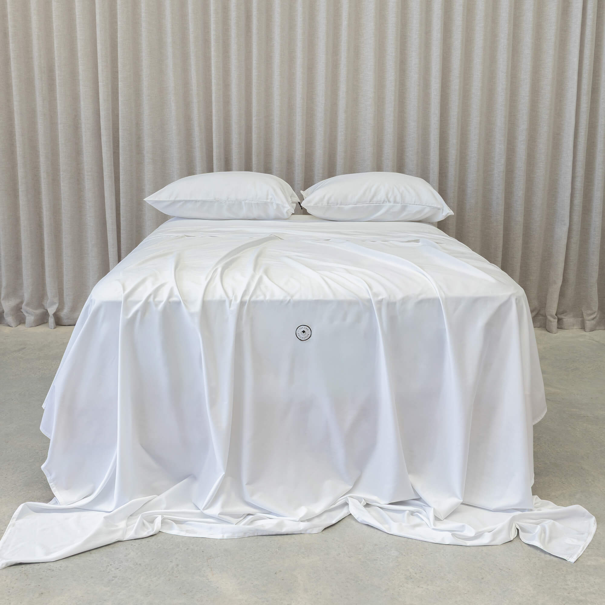 White bedspread with a logo on a bed against a neutral background