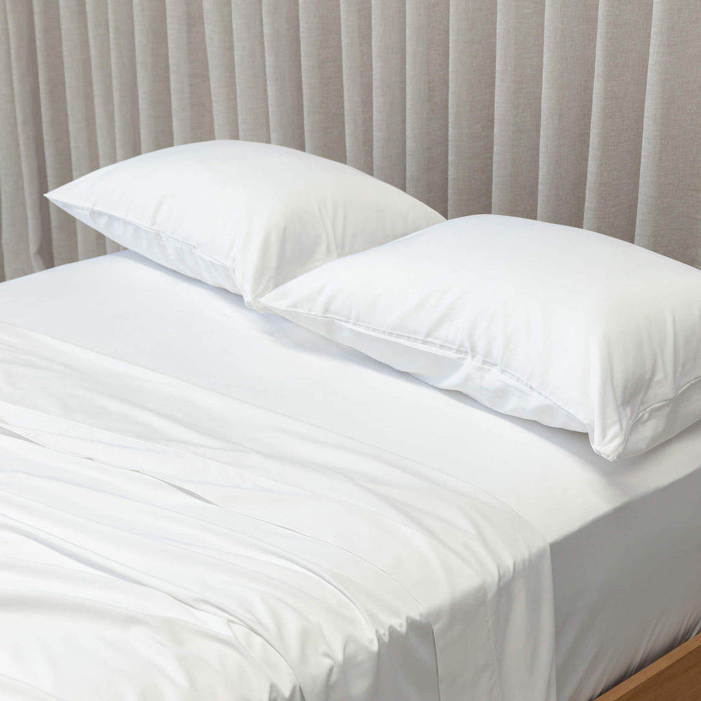 White bedspread on a bed with pillows against a beige curtain background