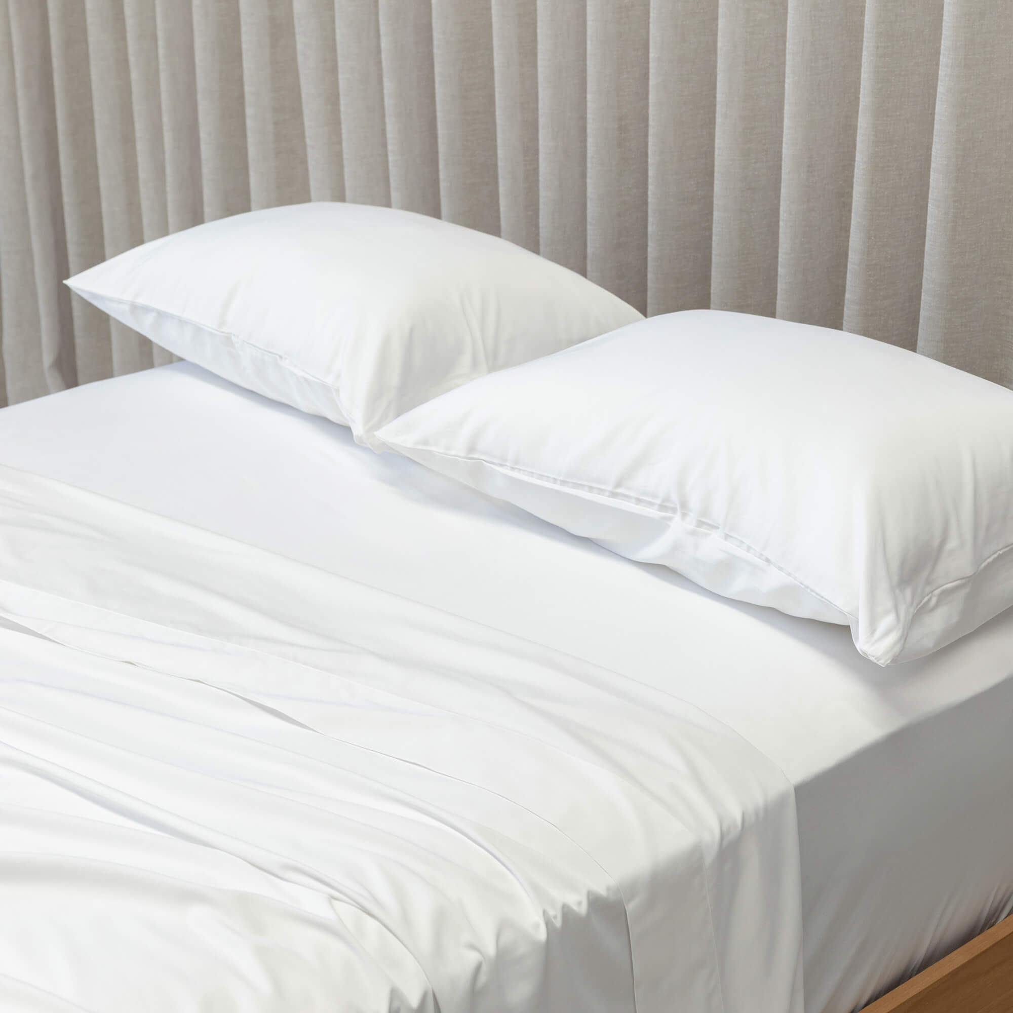 White bedspread on a bed with pillows against a beige curtain background