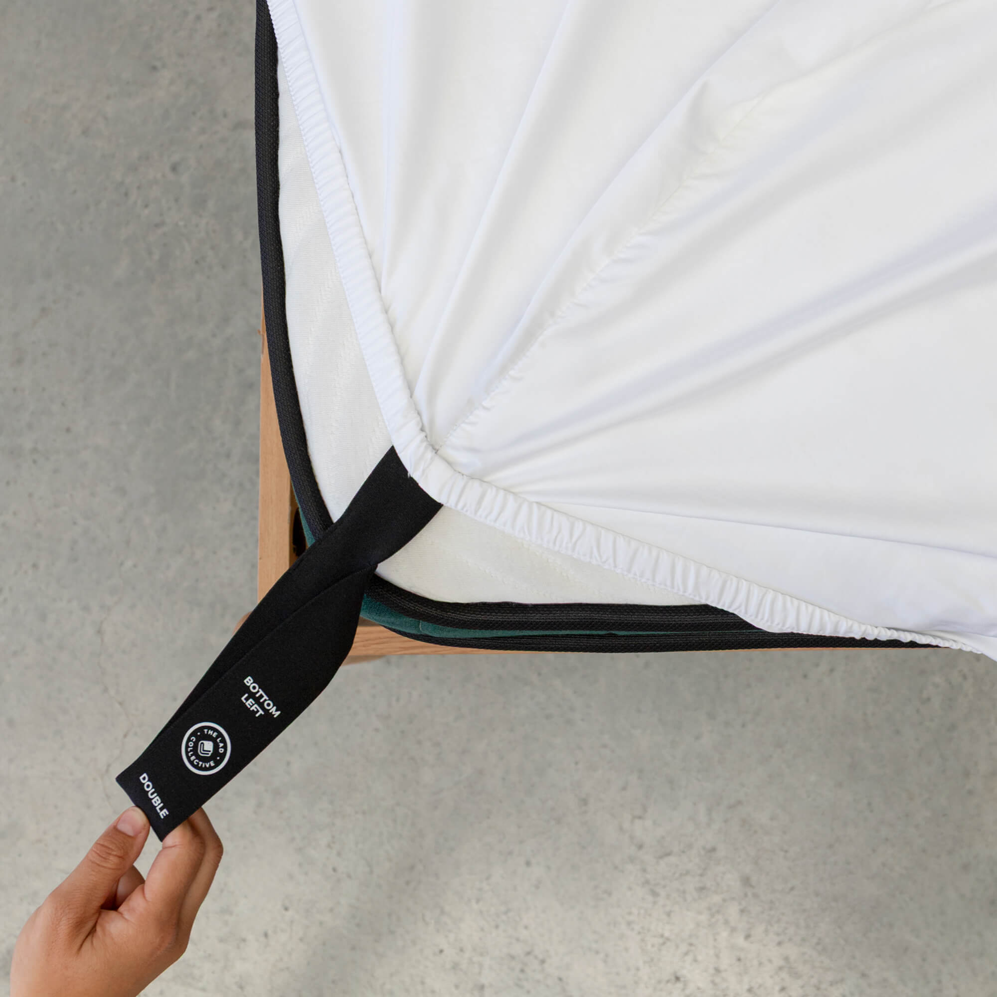 Person holding a black strap with a brand logo on a white mattress.