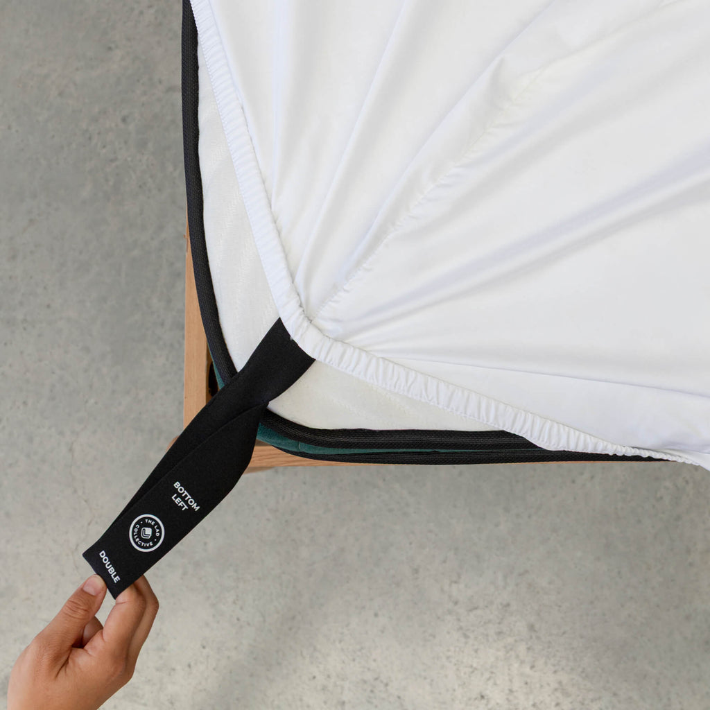 Person holding a black strap with a brand logo on a white mattress.