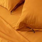 Close up of orange pillowcases with zipper detail on orange bedspread.
