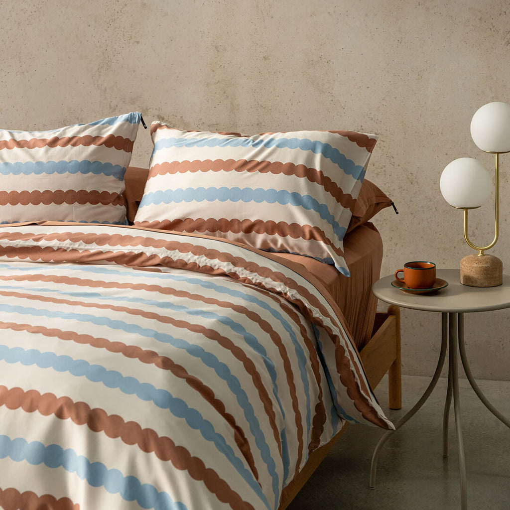 Bed with striped bedding and pillows in a room setting with a side table and lamp.