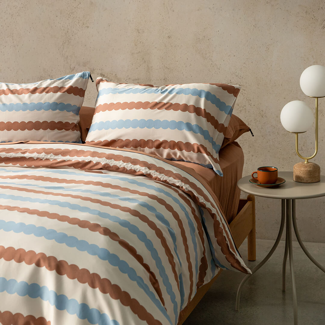 Bed with striped bedding and pillows in a room setting with a side table and lamp.