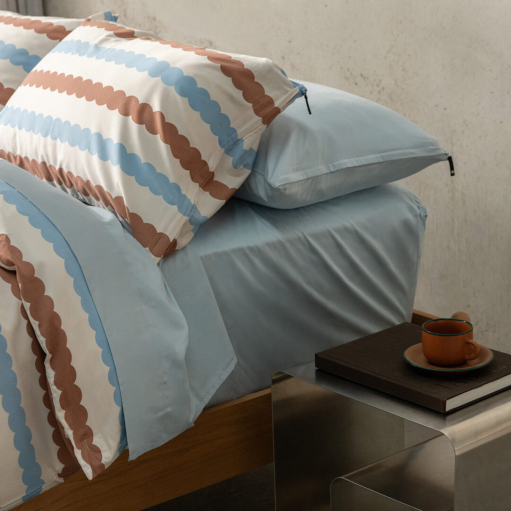 Bed with striped bedding and pillows, nightstand with a book and cup in the foreground.