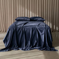 Navy blue satin bedspread on a bed with matching pillows against a beige curtain background.