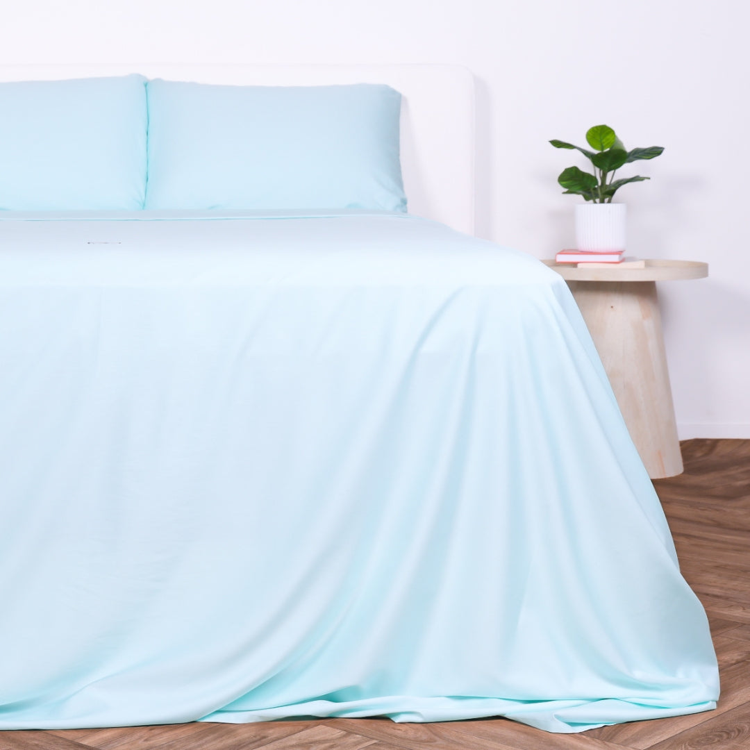 Riviera Blue bed set with draped sheet and matching pillows on a white bed frame.