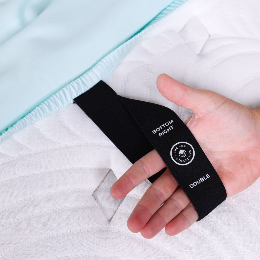 Close-up of labeled corner strap on a fitted sheet showing ‘Bottom Right’ and ‘Double’ for easy bed making.
