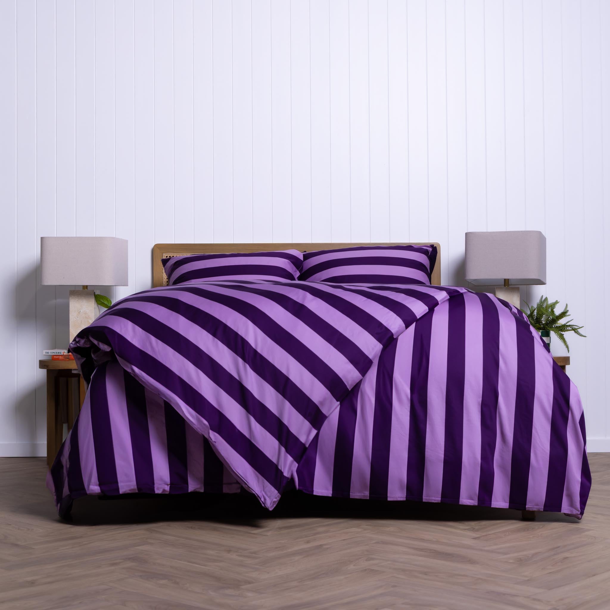 Purple and lilac striped bedding set on a bed with a white wall background.