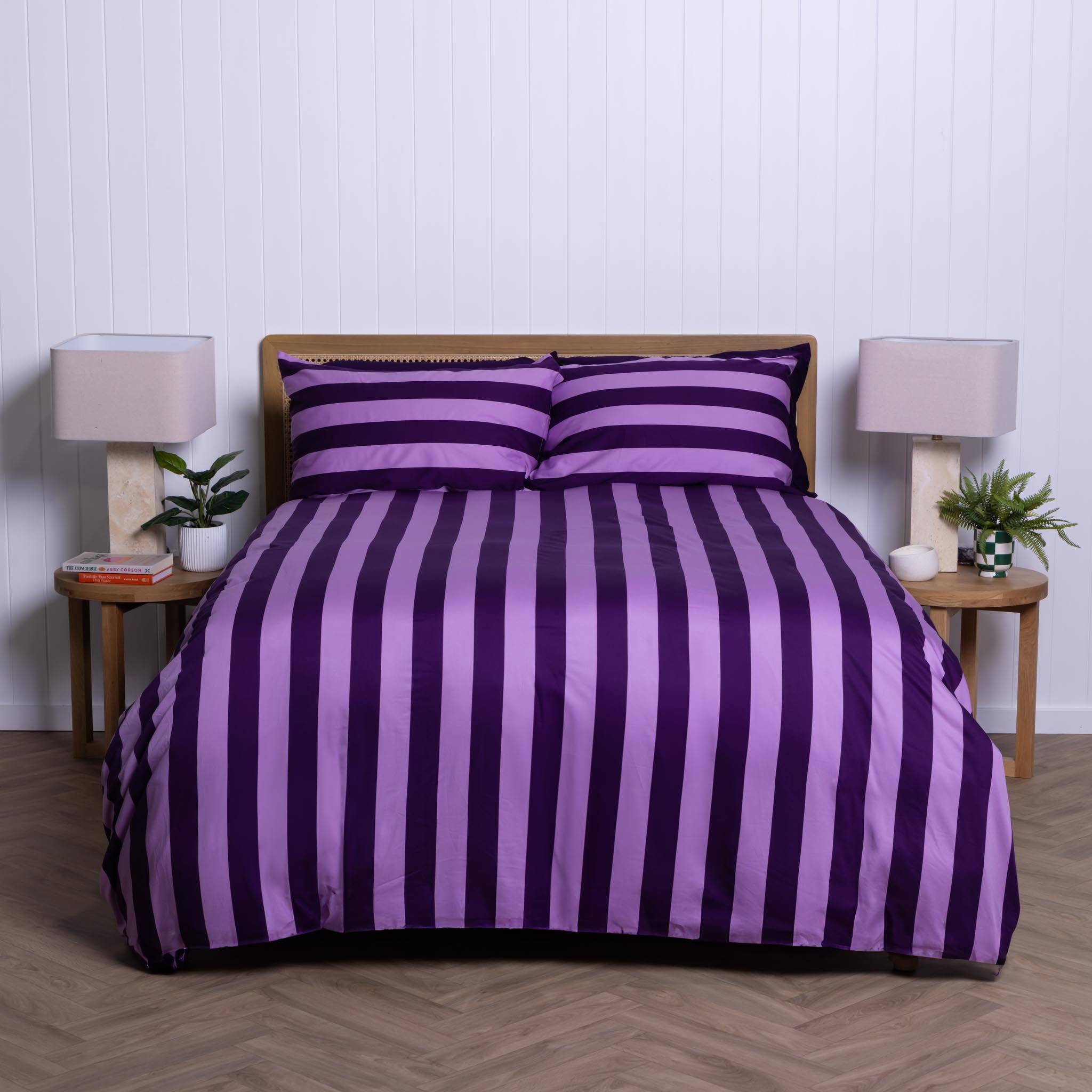 Purple and lilac striped bedding set on a bed with matching pillows, in a bedroom setting.