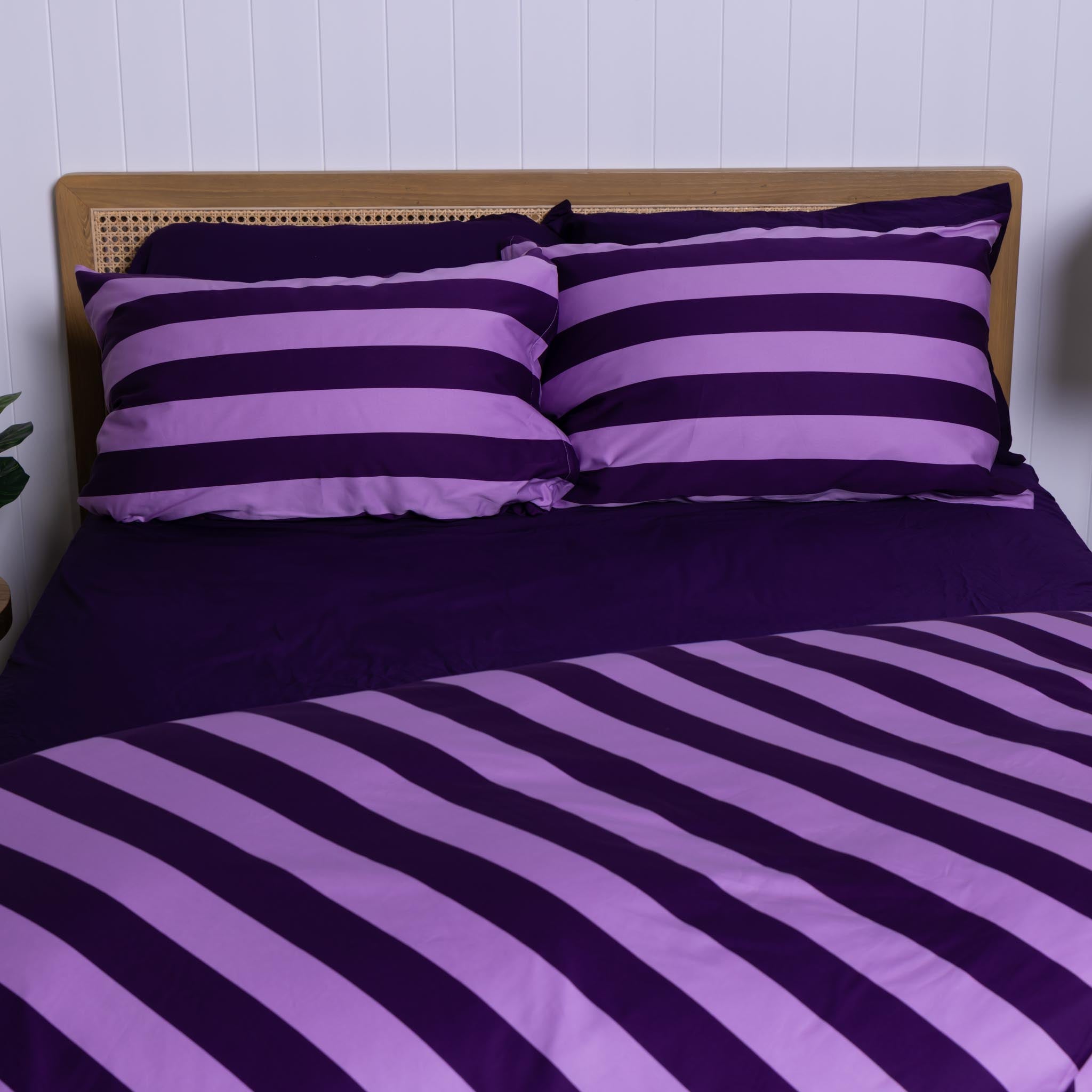 Lilac and dark purple striped bedding set on a bed with a wooden headboard.