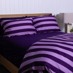 Lilac and dark purple striped bedding set on a bed with a wooden headboard - shown on an angle.