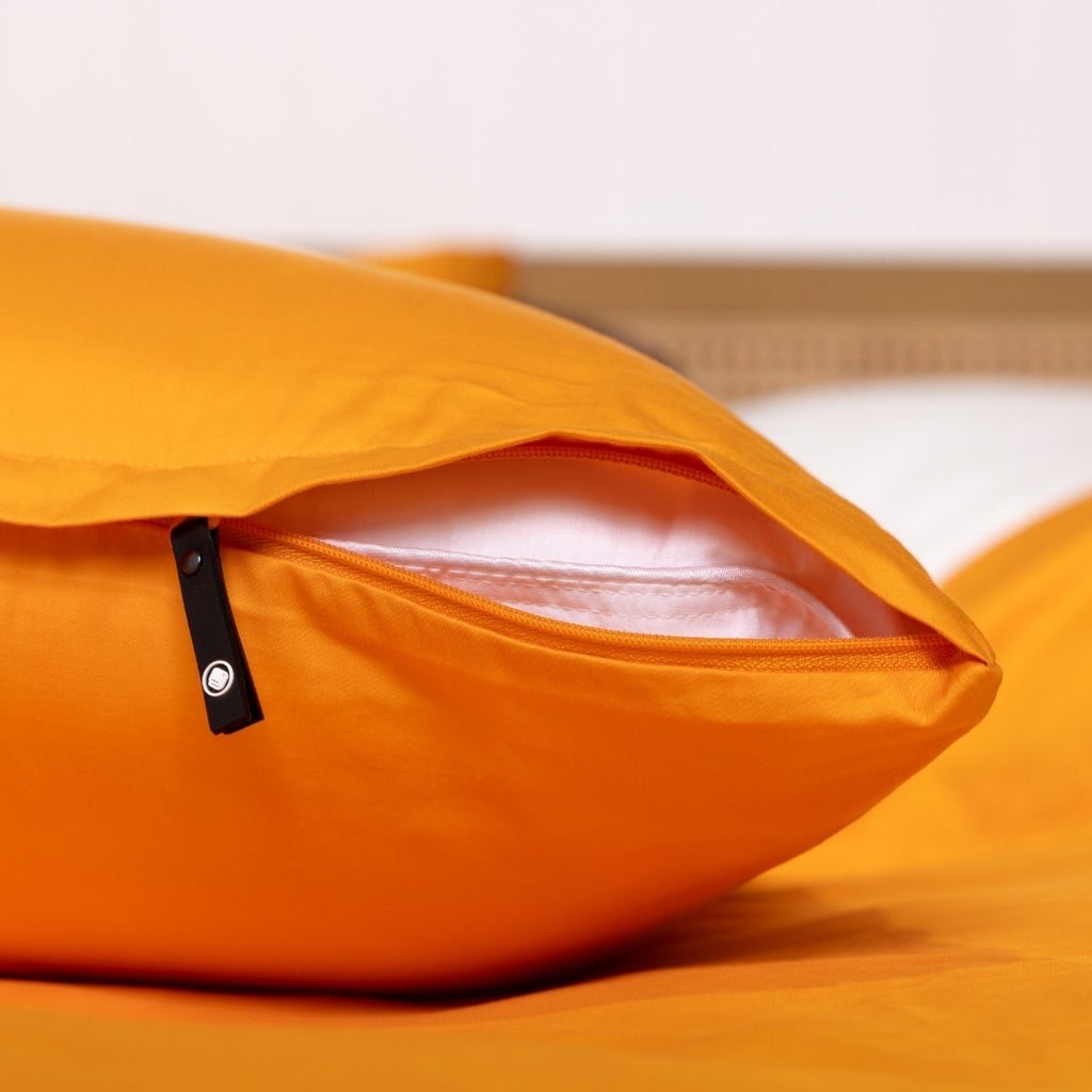 Close-up of an orange pillow with a clear window on a bed.