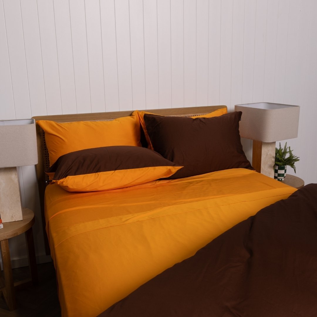 Bed with orange and brown bedding set against a white paneled wall.