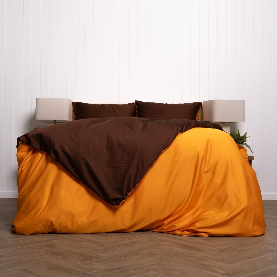 Bed with brown and orange bedding against a white wall.