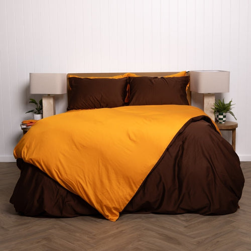 Bed with orange and brown bedding set against a white wall.