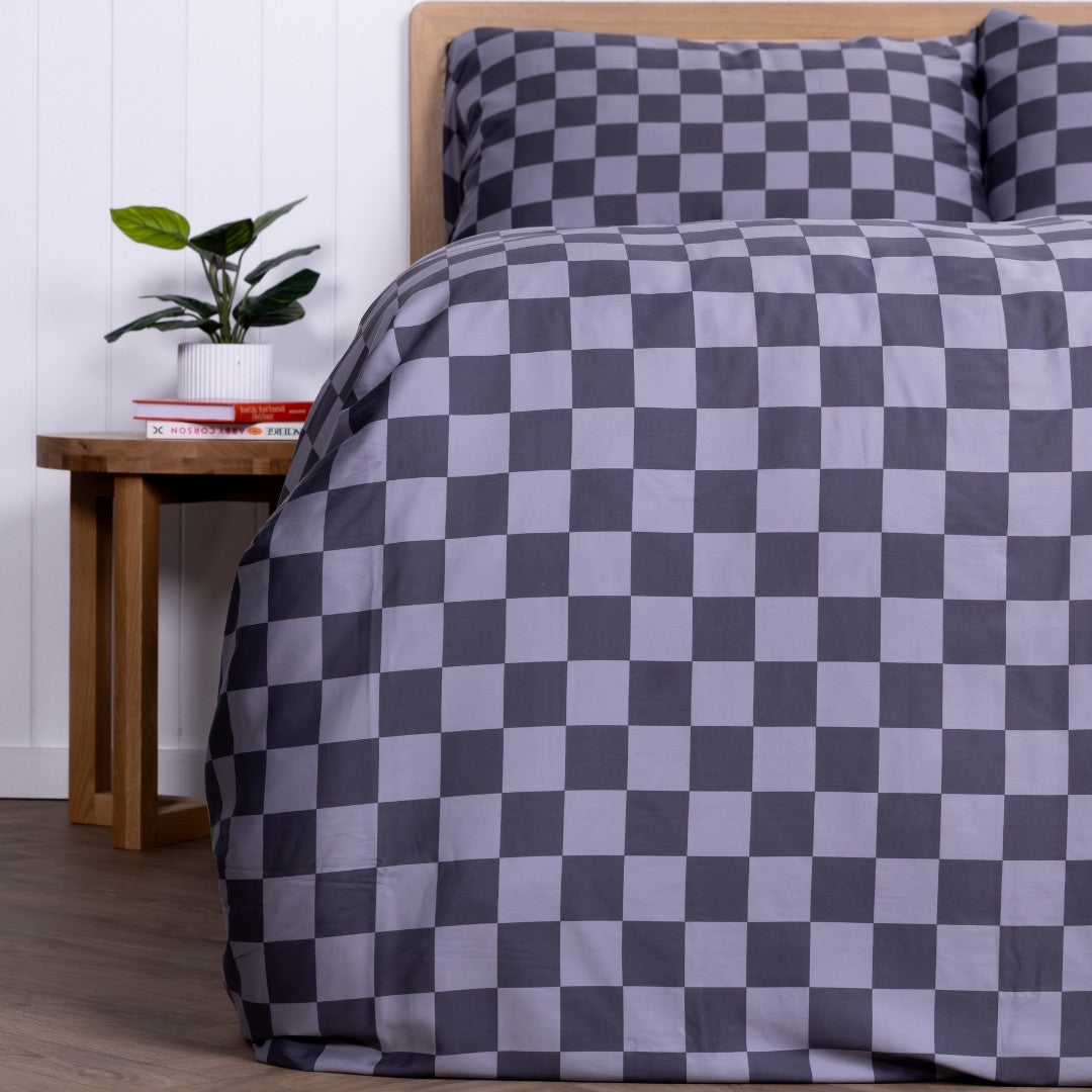 Checkered duvet cover and pillowcases on a bed with a wooden side table and plant in the background.