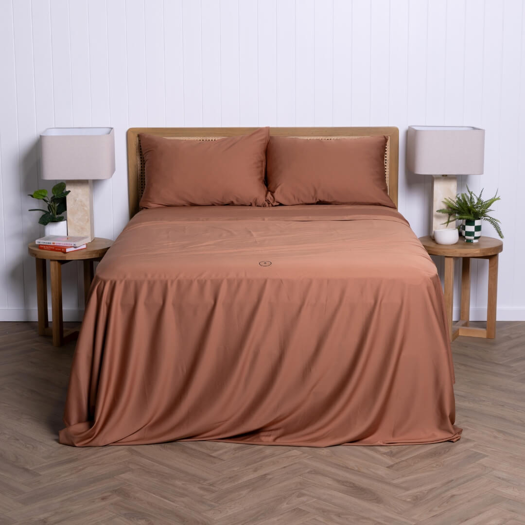 Full view of a neatly styled bed with rust-coloured bamboo-cotton bedding set by The Lad Collective.