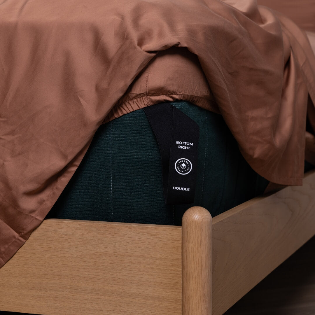 Elastic corner strap labelled ‘Bottom Right’ and ‘Double’ on a dark green mattress under rust-coloured sheets.