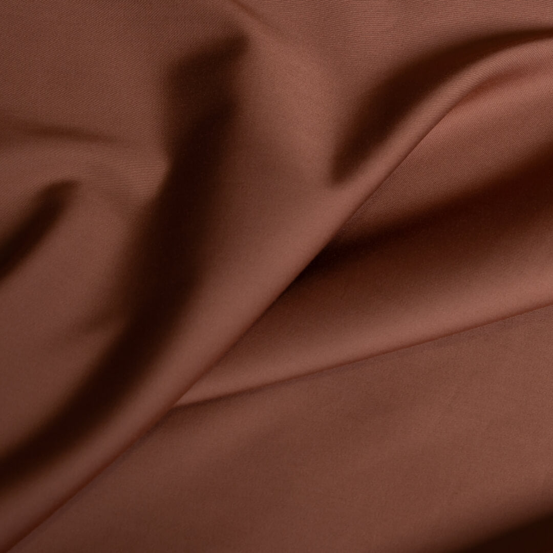 Close-up texture shot of soft rust-coloured bamboo cotton sheet fabric with natural folds.