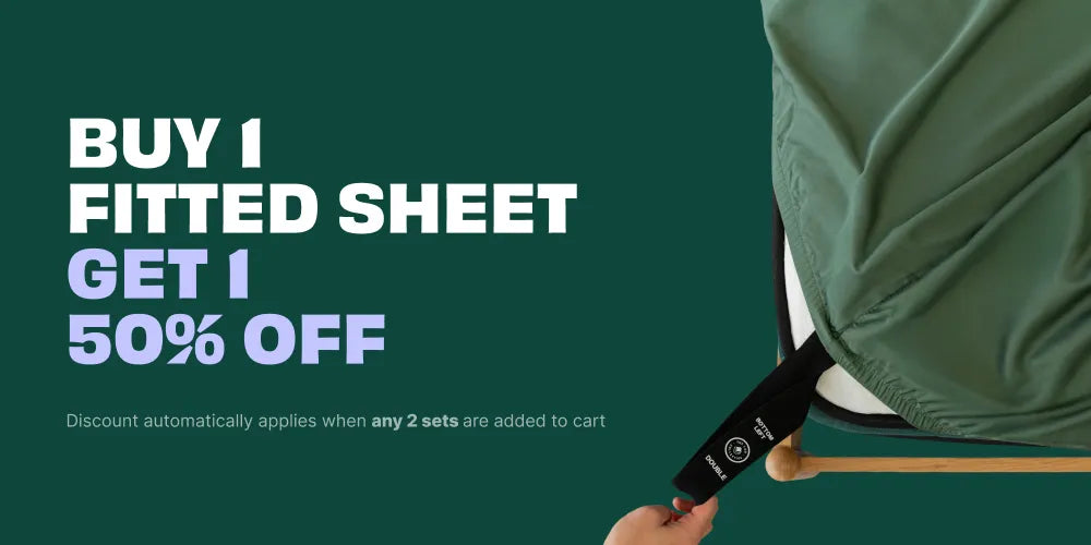 Promotional graphic for a fitted sheet offer, featuring a hand adjusting a dark green fitted sheet on a bed corner against a dark green background with white and purple text that reads 'BUY 1 FITTED SHEET GET 1 50% OFF'.