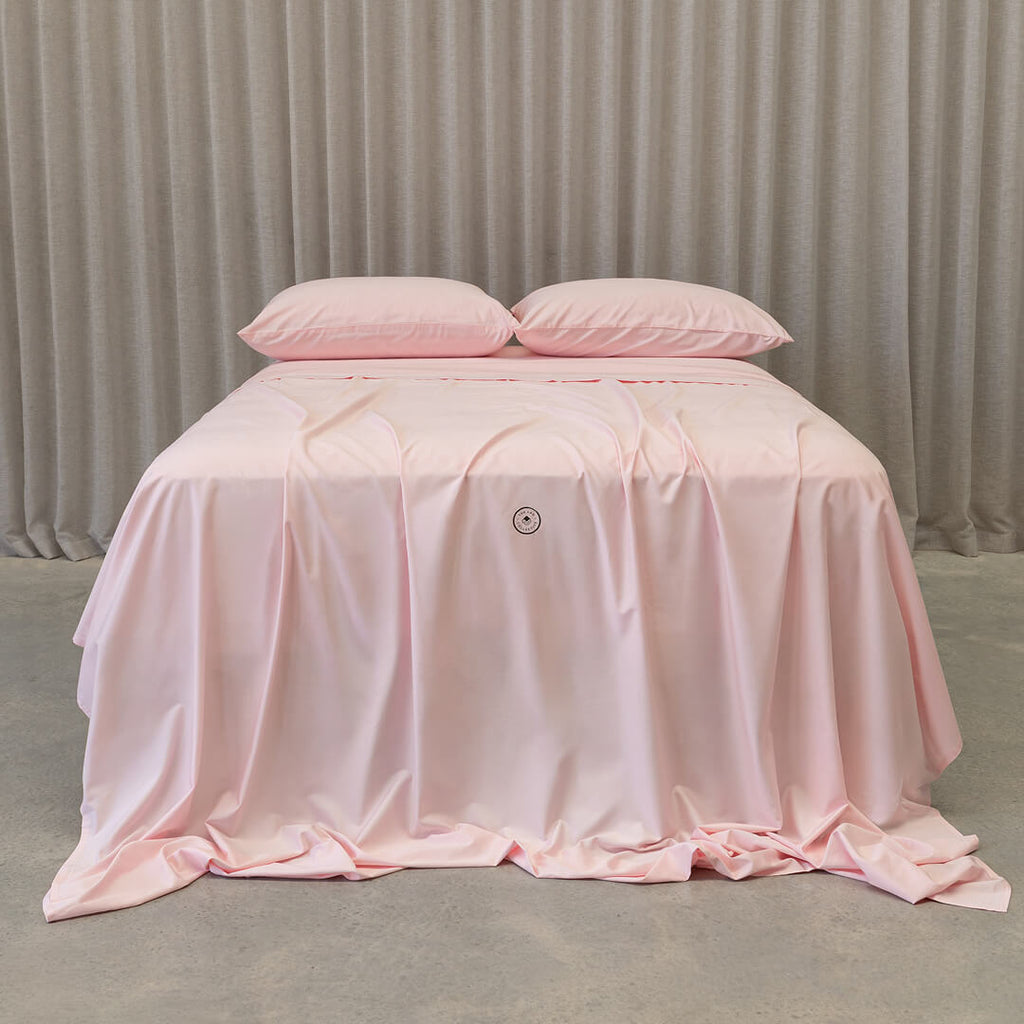Soft pink bedding set on a bed, against a neutral background.