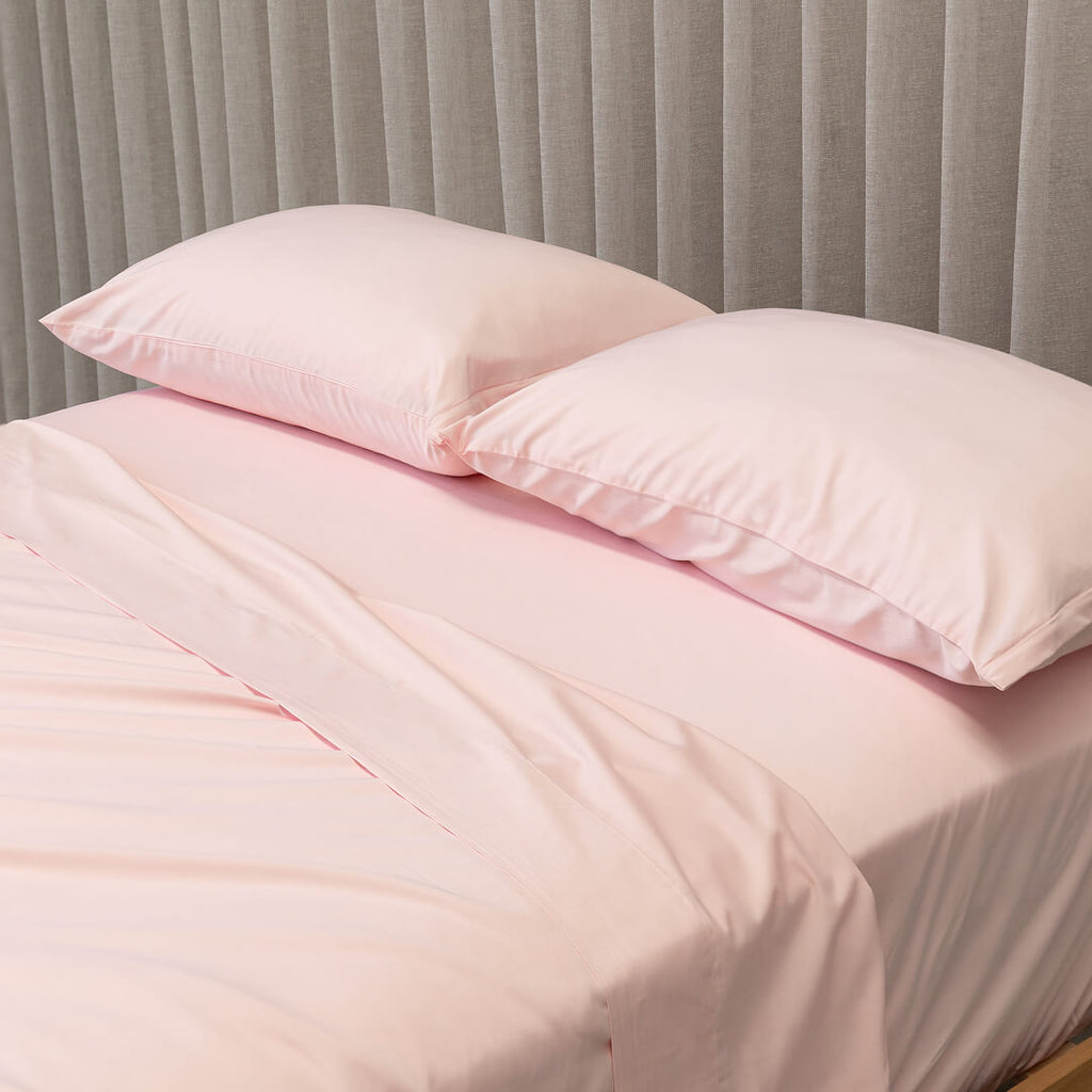 Pink bedding set with two pillows on a bed against a gray curtain background.