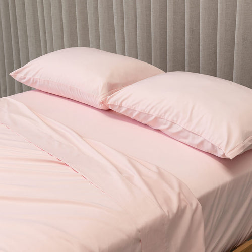 Pink bedding set with two pillows on a bed against a gray curtain background.