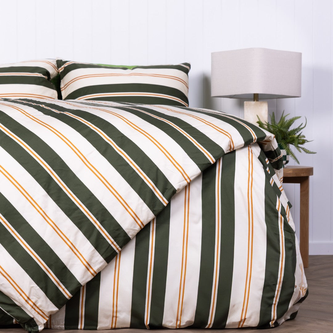 Striped green and white comforter on a bed with a lamp and plant in the background.