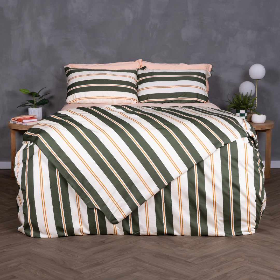 Front-facing view of a bed dressed in the Lake Tahoe Magnetic Clip & Zip Duvet Cover. The bold striped design in green, cream, and amber commands attention, with matching pillowcases and light peach sheets peeking through at the top.