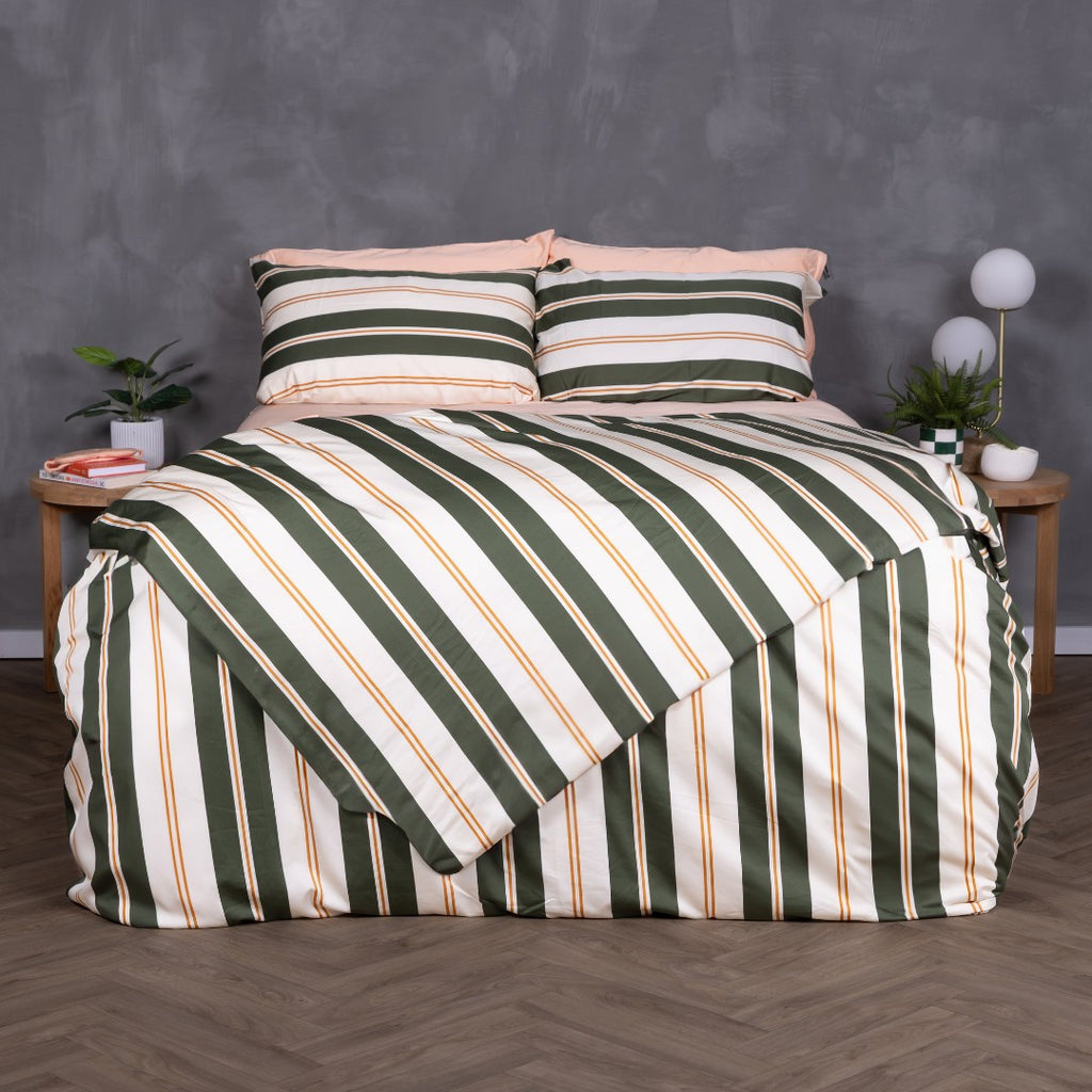 Front-facing view of a bed dressed in the Lake Tahoe Magnetic Clip & Zip Duvet Cover. The bold striped design in green, cream, and amber commands attention, with matching pillowcases and light peach sheets peeking through at the top.