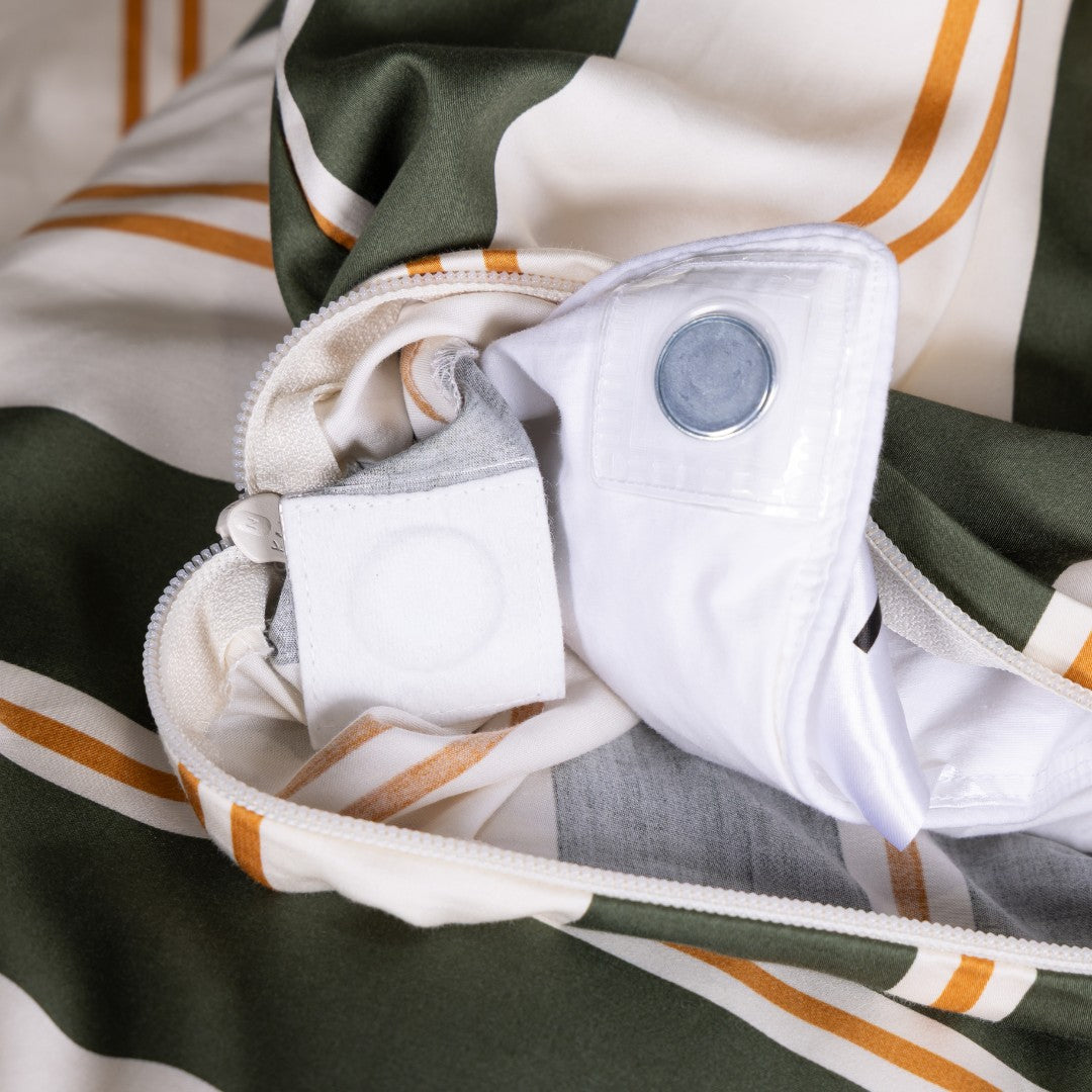 Close-up of a folded garment with a white shirt and gray pants inside, on a striped fabric background.
