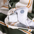 Close-up of a folded garment with a white shirt and gray pants inside, on a striped fabric background.