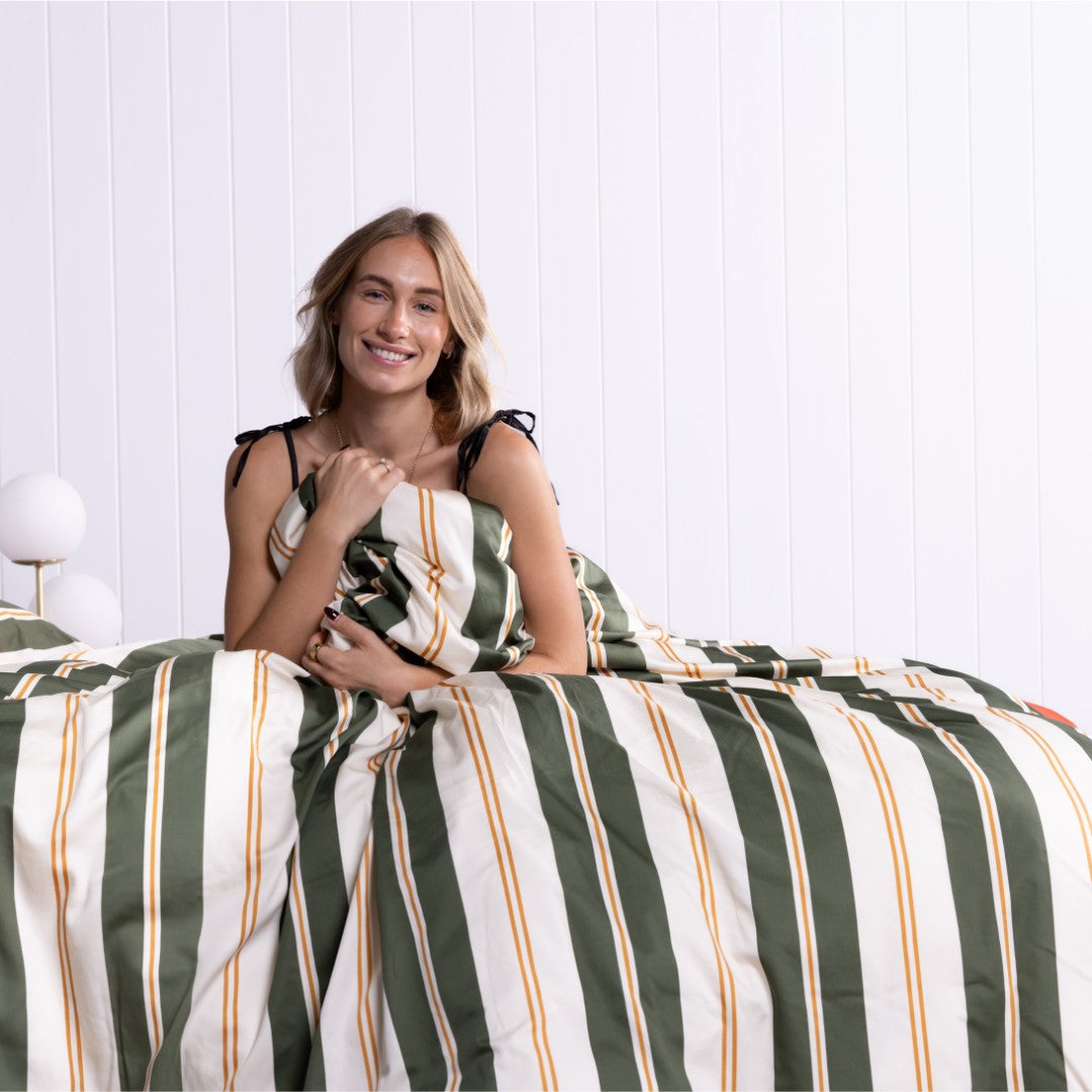 Woman sitting on a bed with striped bedding against a white wall