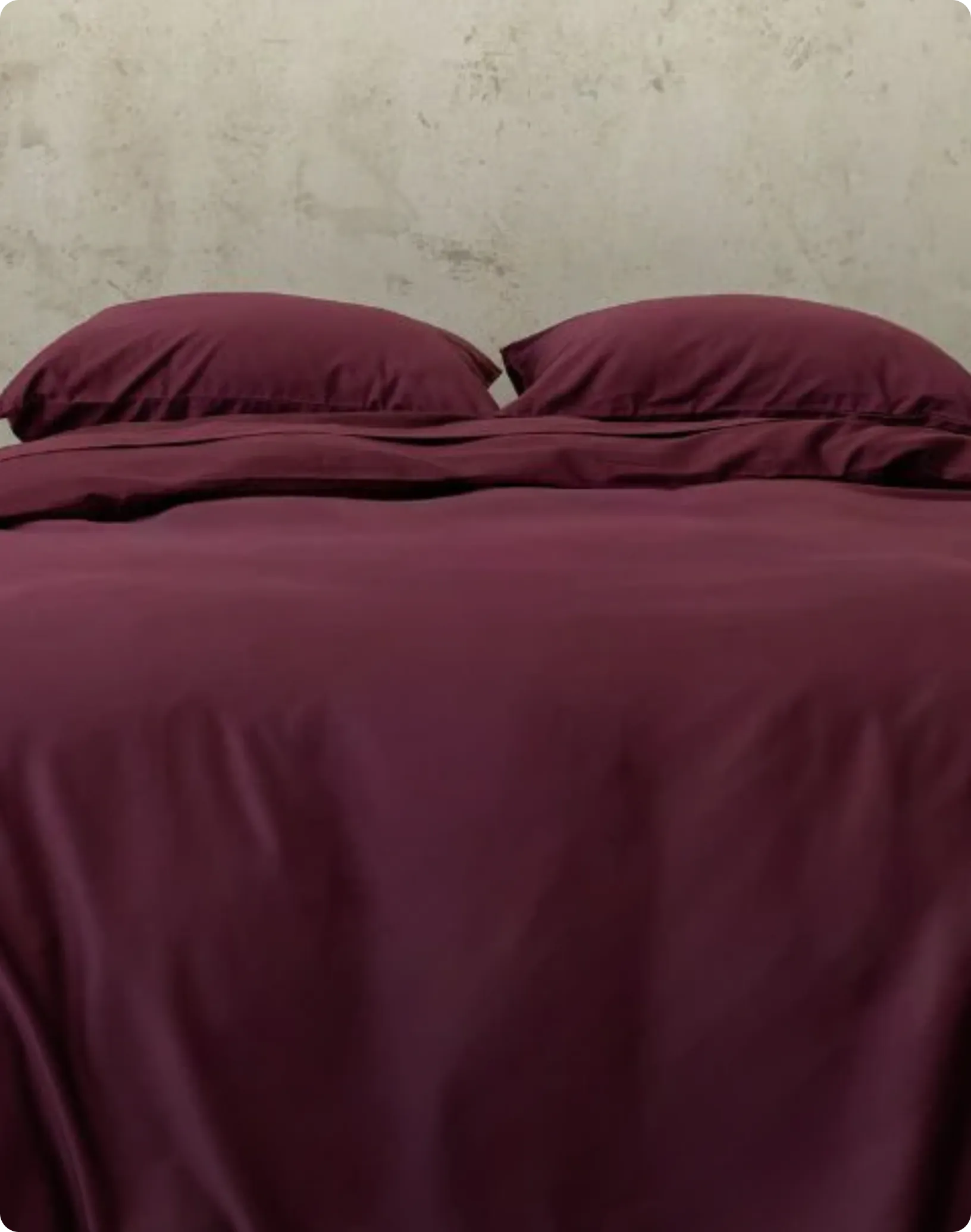 Burgundy bedding set on a bed with a neutral headboard.
