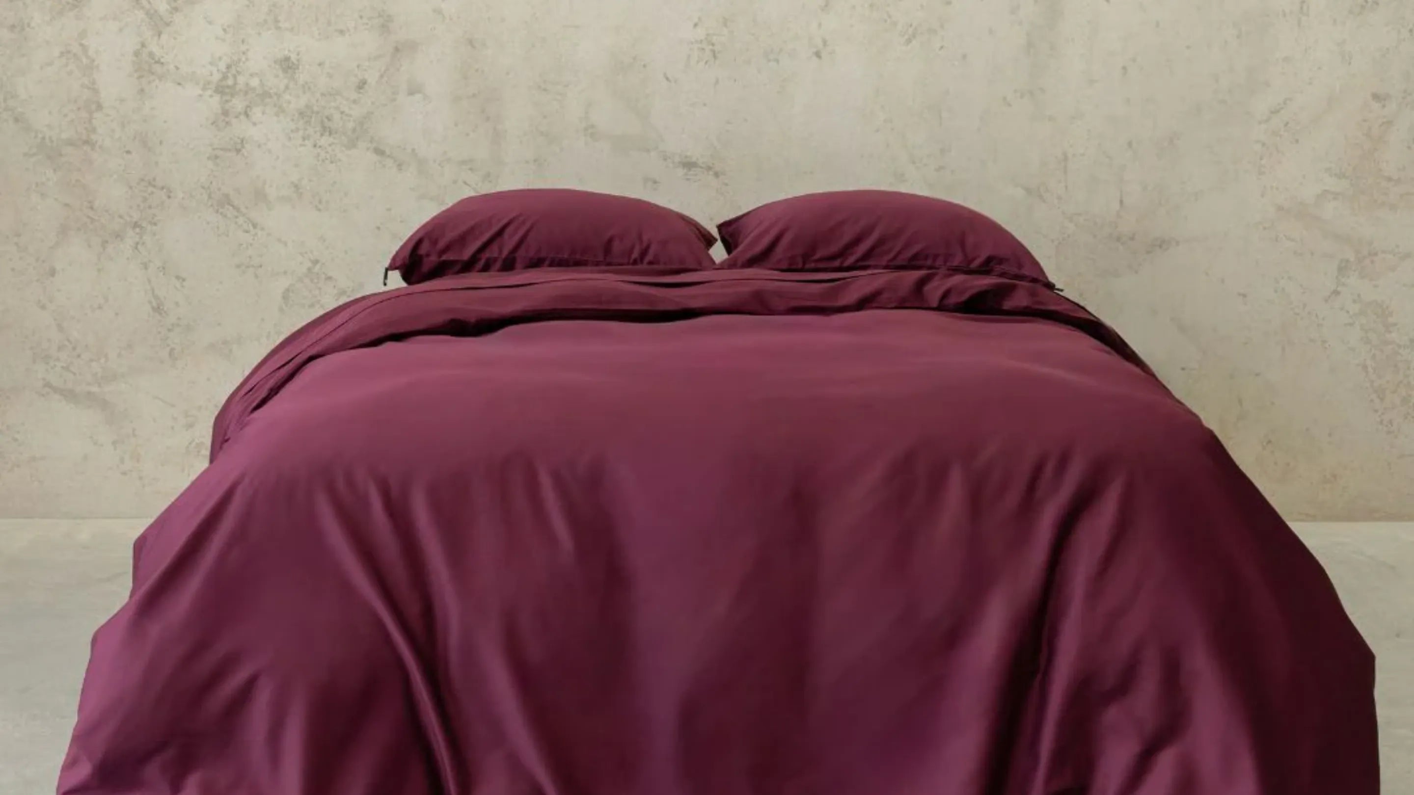 Maroon comforter on a bed against a beige wall