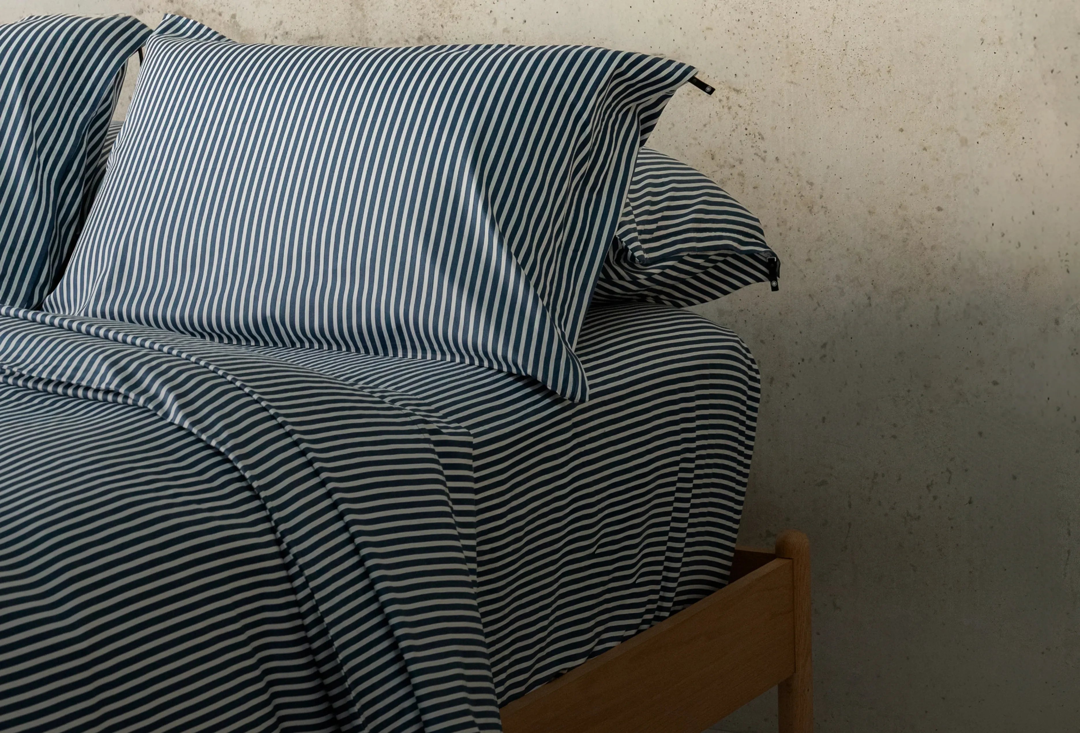 Striped bed sheets and pillows on a wooden bed against a textured wall.