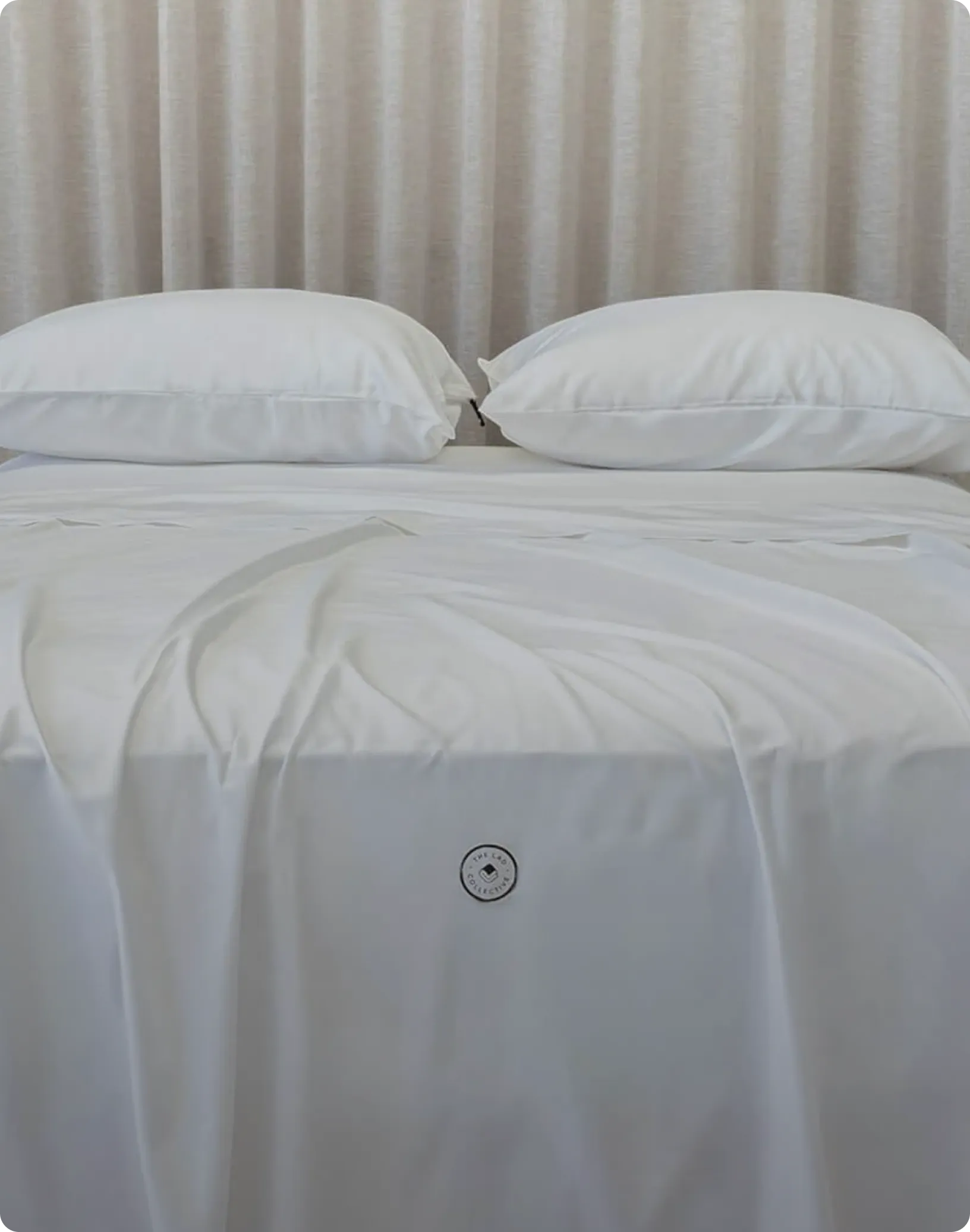 White bedspread with a small circular logo on a bed against a white curtain background